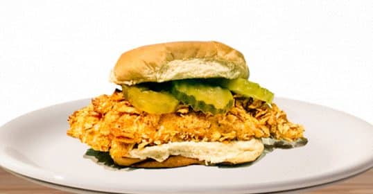 Healthy crispy chicken sandwich with pickles on a white plate.