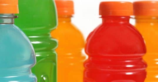 Assorted colorful sports drink bottles, rich in electrolytes for health, are lined up in a row with a focus on the caps and upper sections.