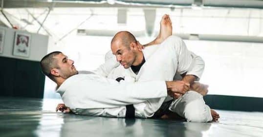 Two individuals overcoming obstacles through practicing Brazilian Jiu-Jitsu in a gym.