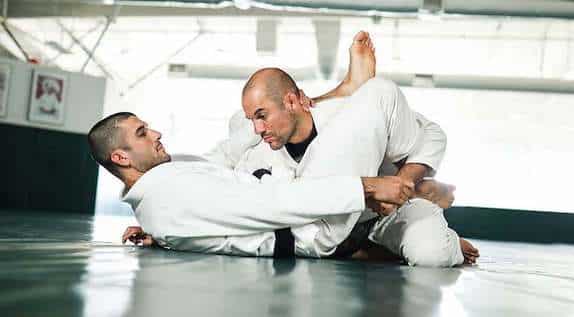 Two individuals overcoming obstacles through practicing Brazilian Jiu-Jitsu in a gym.