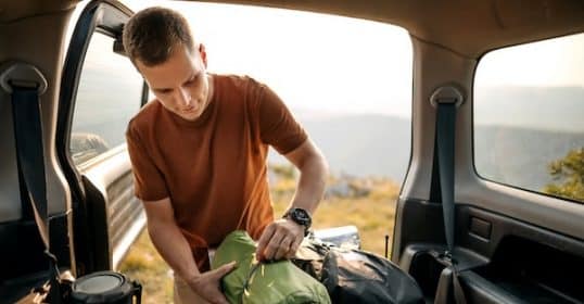 Man packing camping gear into a vehicle at dusk.