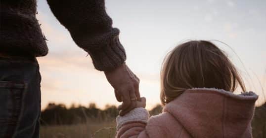 Father holding his daughter's hand outdoors at dusk, embodying the father-daughter relationship.
