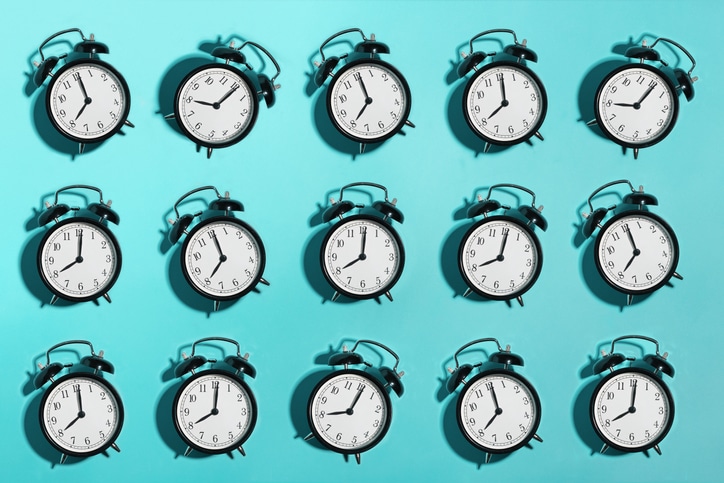 An array of identical black alarm clocks against a teal background, each showing a different time, symbolizes the real reason behind procrastination discussed in Podcast #931.