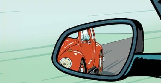 A red vintage car reflected in a vehicle's side mirror, adjusted to eliminate blind spots.
