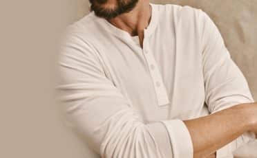 Man in a white long-sleeve Henley shirt with folded arms, showcasing one of the stylish ways to wear it.