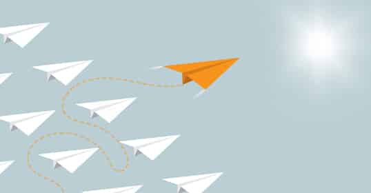 A lone orange paper plane, embodying leadership qualities, leads a group of white paper planes on a different flight path toward the bright sun.