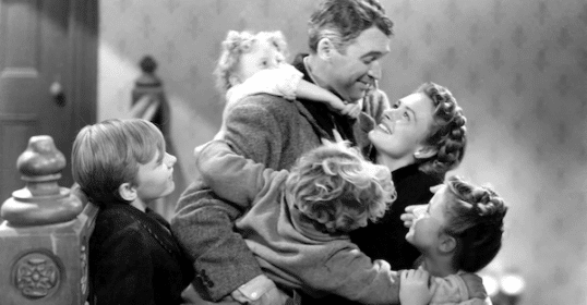 A black and white photo of a happy family moment with two adults and three children embracing each other affectionately after watching classic Christmas movies.