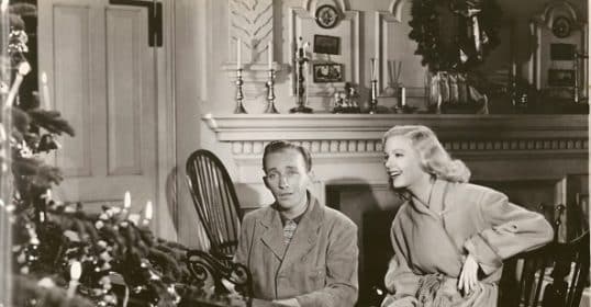 Two people in vintage attire from the 1940s sitting by a piano near a Christmas tree, enjoying classic Christmas songs in a classic black-and-white film scene.