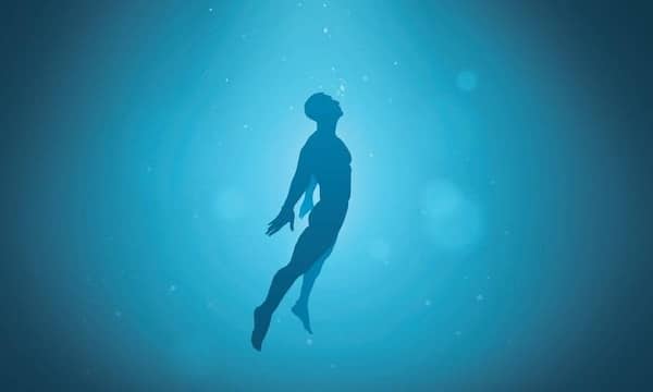 Silhouette of a person swimming underwater with light rays shining through the water, exploring the Science of Immersion.