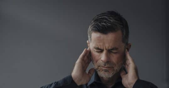 Man with closed eyes massaging his temples, possibly seeking tinnitus relief or indicating a headache or stress.