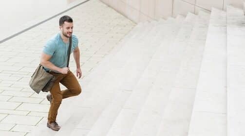 Man ascending outdoor stairs with a shoulder bag, listening to Podcast #955.