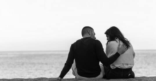 A black and white photo of a couple sitting on the beach.