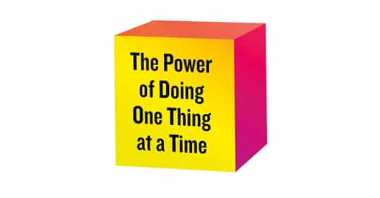 A yellow and red cube with the phrase "the power of doing one thing at a time" written on it, featured in Podcast #975.