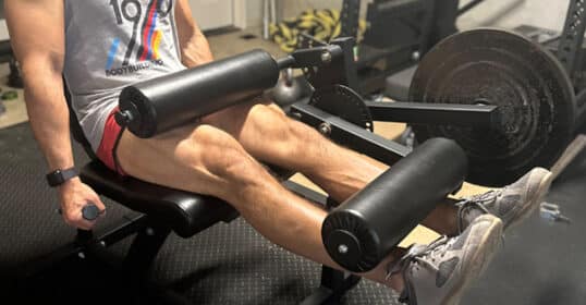 A person using a leg extensions machine at a gym, focusing on the lower body exercise with visible effort.