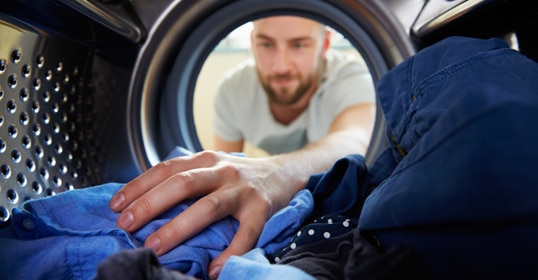 Man doing laundry, reaching inside a washing machine for clothes.