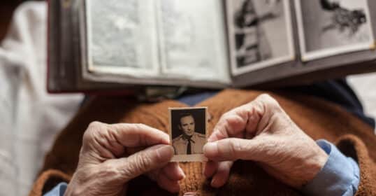 Elderly person holding a small, old photograph in front of an open photo album, recovering nostalgic memories.