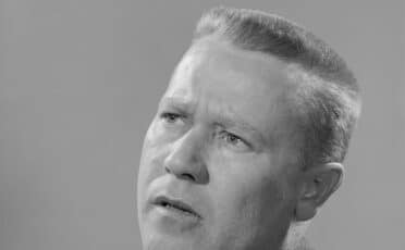 A black and white portrait of a man in a suit and tie with a contemplative expression, looking slightly upwards, radiates an aura of metacognition.