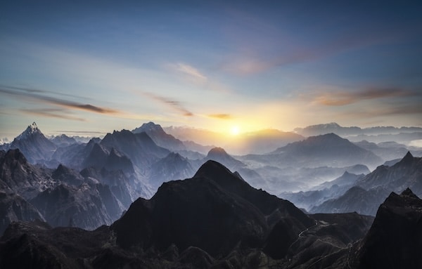 A panoramic view of a mountainous landscape at sunrise, with layers of rugged peaks and ridges extending into the distance under a clear sky, as if each mountain represents a step in personal development.