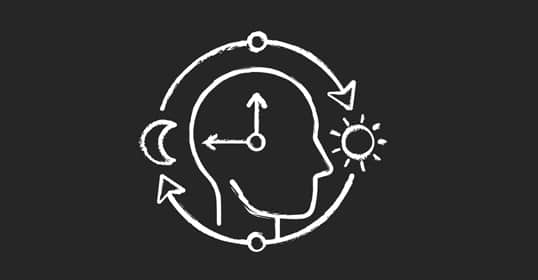 Chalk drawing of a human head with a clock face inside, surrounded by arrows, a crescent moon, and a sun on a black background, symbolizing circadian rhythm and its role in health and better sleep.