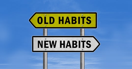 Two directional signs against a blue sky point the way: one reads "Old Habits" in yellow, and the other reads "New Habits" in white. It's like tuning into a podcast on habit change, guiding you to build better behaviors for a brighter future.