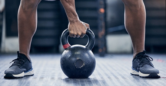 Faithful to their fitness journey, the person lifts a heavy kettlebell in the gym, sporting blue athletic shoes.