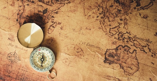 A vintage brass compass rests on an aged parchment world map, featuring continents and nautical symbols, inviting one into the unknown with themes of exploration and navigation.