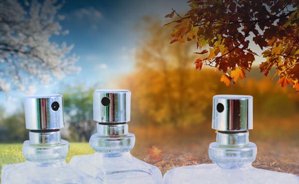 Three perfume bottles with silver spray tops are set against a background split between spring blossoms and autumn leaves, highlighting a selection of men’s cologne that makes for the perfect signature fragrances.