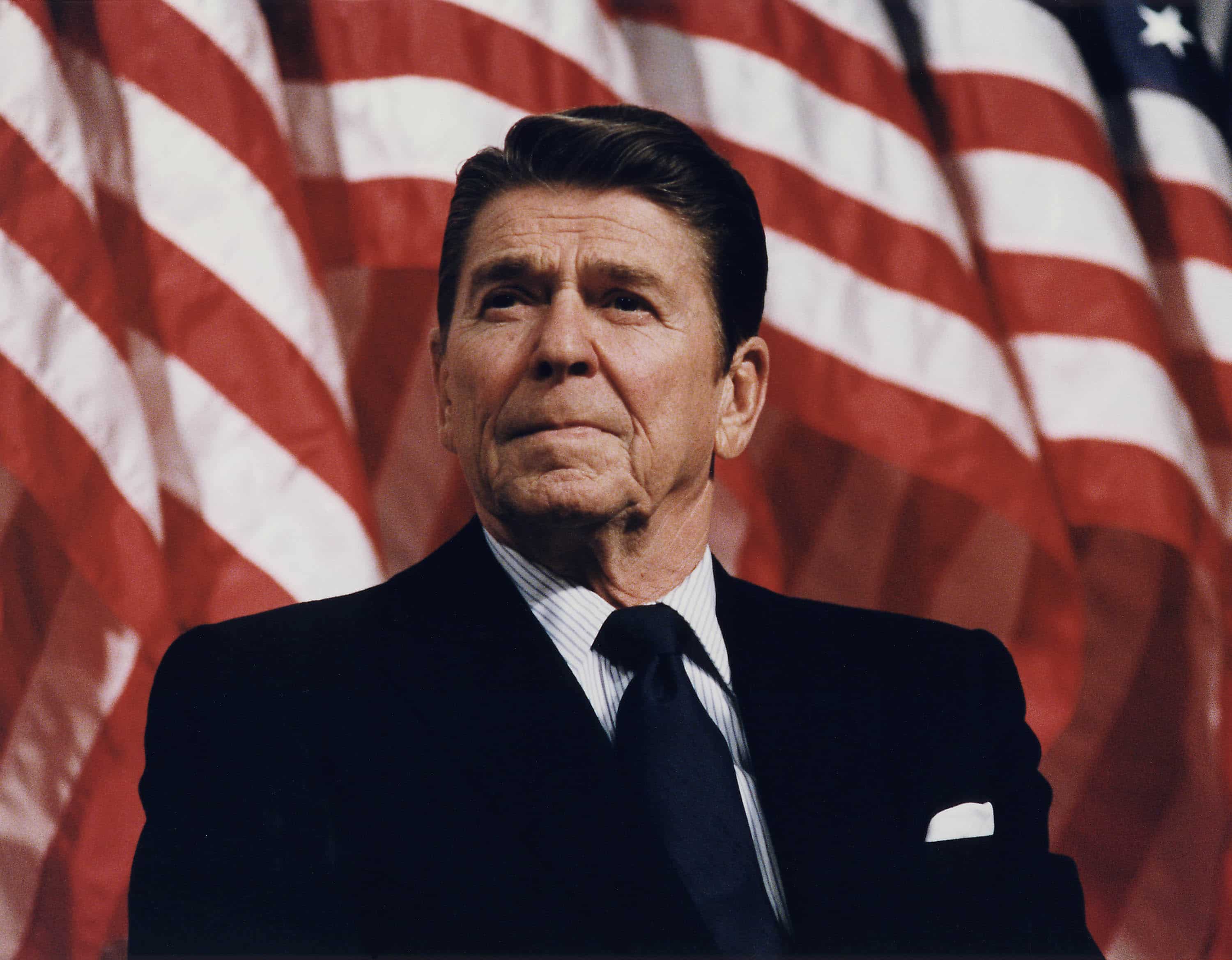 Ronald Reagan standing in front of flag.