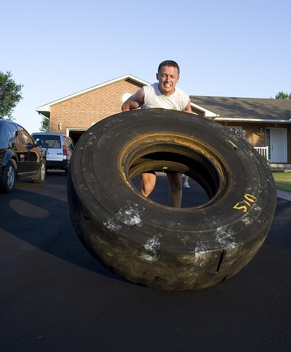 Man flipping tractor tire on road.