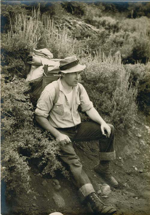 Vintage man wearing backpack while sitting in the brushes.