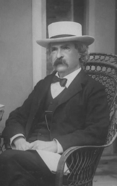 Mark Twain wearing bowtie and hat while sitting on chair.