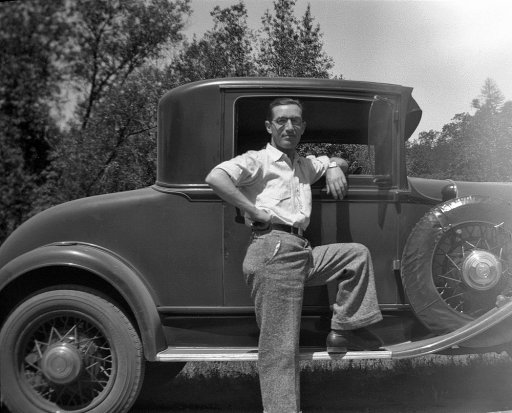 Vintage man standing in front of car in formal dress.