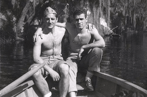 Two vintage shirtless friends posing together in boat on a lake.