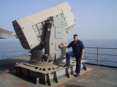 Dan Smith giving pose and standing with US Navy sailor warship.