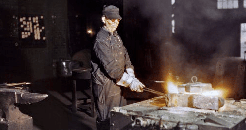 Blacksmith wearing his costume while forging metal in workshop.