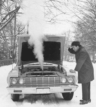 Man looking worry about the steam coming from broken down car in snow.