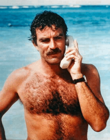 Tom Selleck hearing phone in front of ocean. 