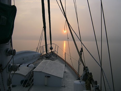 View of sun setting with ocean and sailboat.