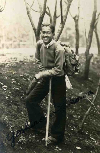 Asian man smiling while hiking outdoors with a stick.
