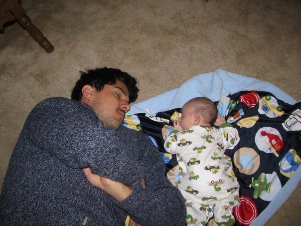A man sleeping with his son on the floor.