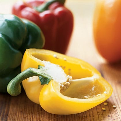 Yellow, green, red and orange bell peppers on cutting board.