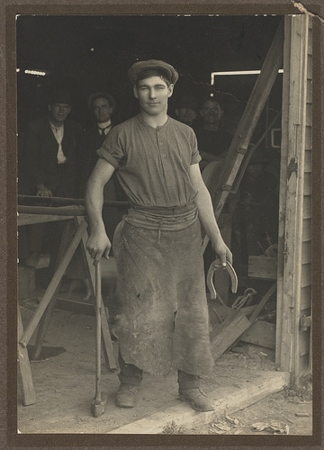 Vintage man wearing apron and holding horseshoe in hand.