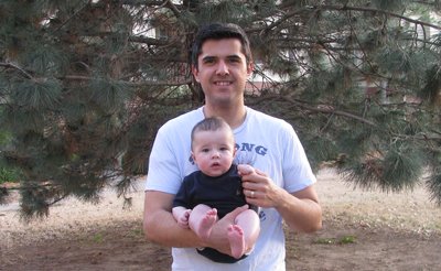 A father carrying his son in front of tree bushes.