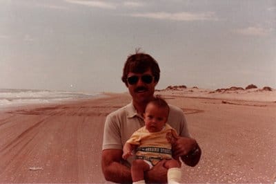 Dad carrying baby on beach. 