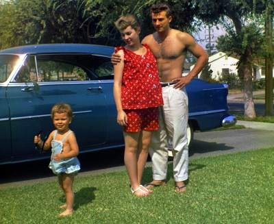 Man standing with his pregnant wife and child in front of car.