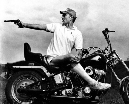 Thompson sitting on motorcycle and pointing the gun.