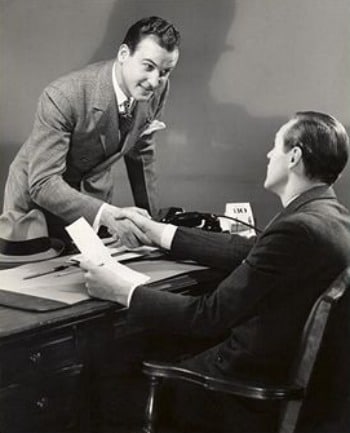 Vintage businessmen shaking hands over desk deal.