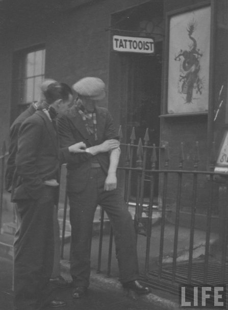 Vintage life magazine men outside tattoo shop and one man holding his arm.
