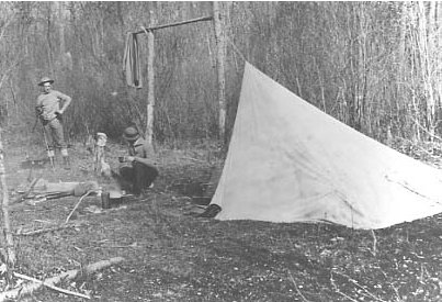 Vintage man camping in woods with tent and campfire.