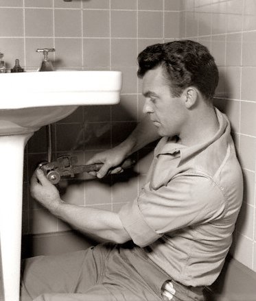 Vintage plumber working on sink sitting on ground.